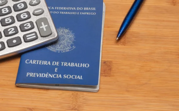 Imagem de uma carteira de trabalho ao lado de uma caneta e calculadora, simbolizando a escala 6x1.